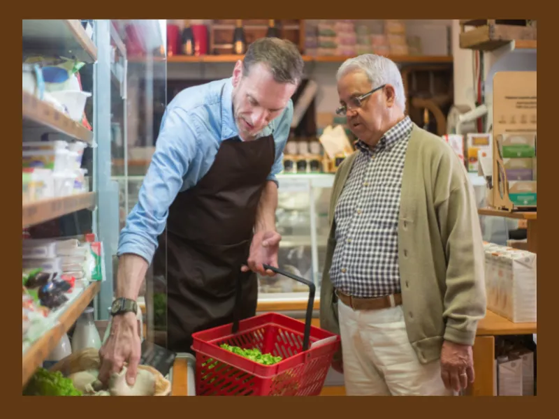 A man is helping an old man to select goods from a grocery store, a referral as a gesture for marketing.
